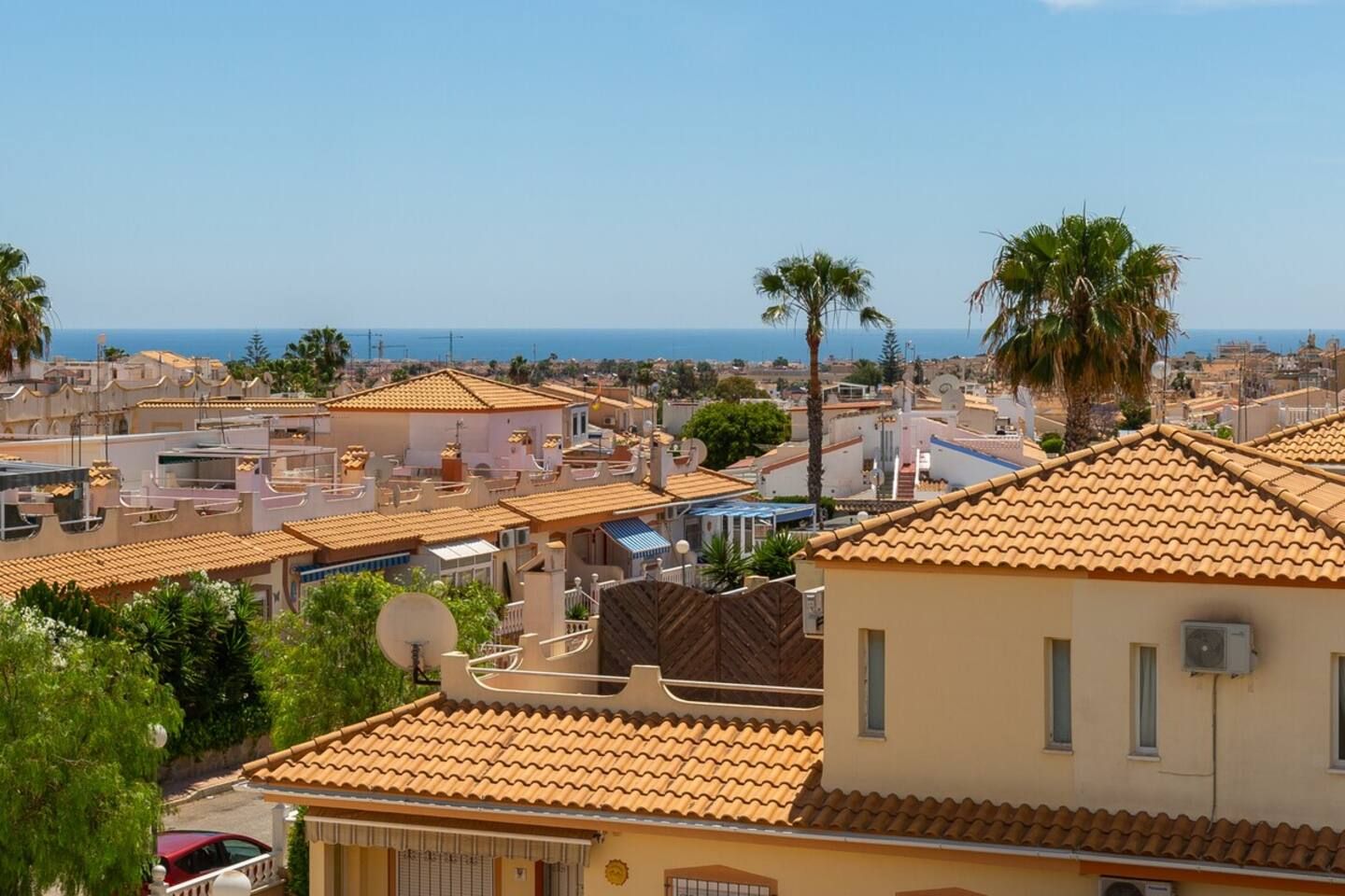 Un quartier résidentiel caractérisé par des toits recouverts de tuiles en terre cuite, des palmiers et une vue dégagée sur la mer.