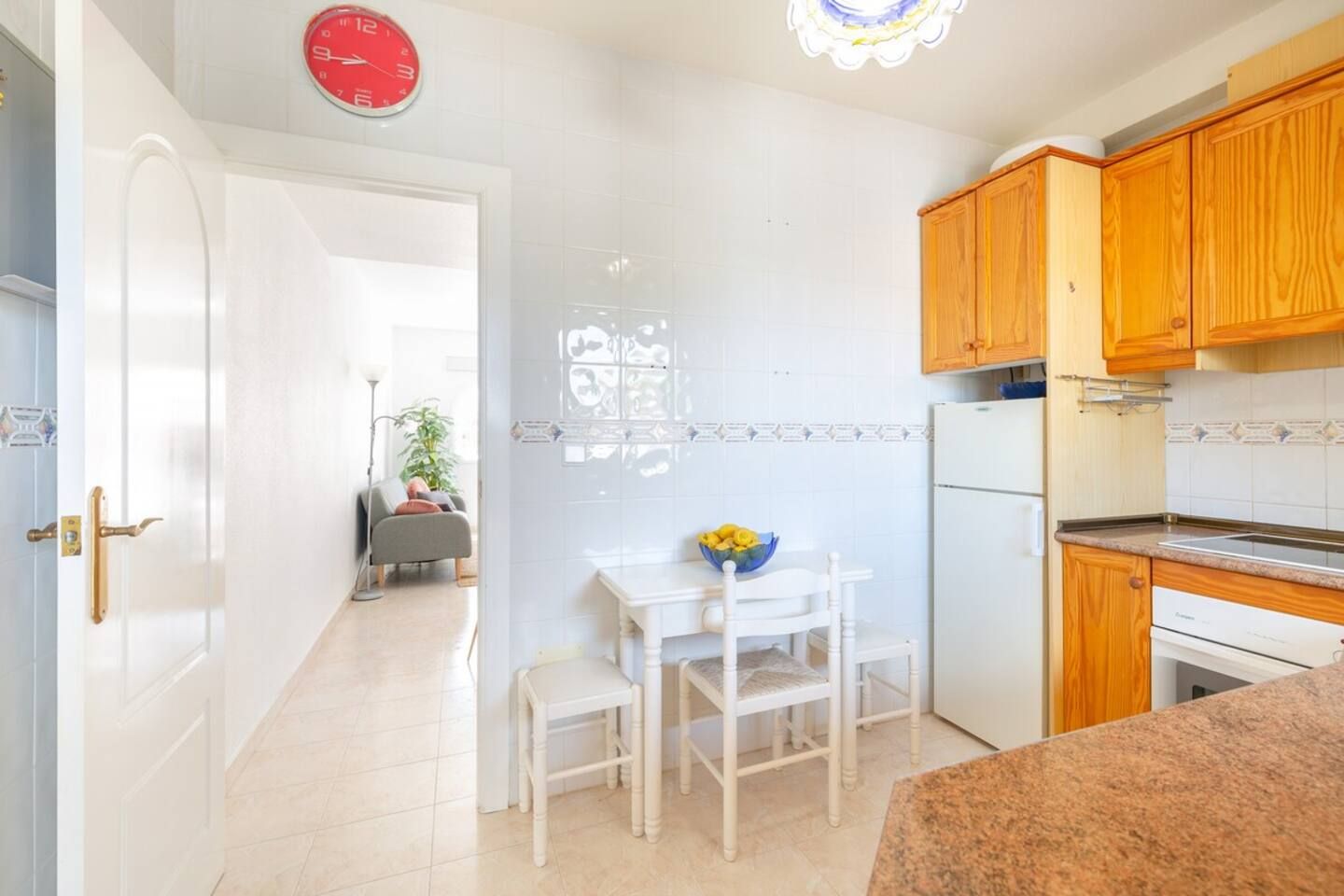 A kitchen with wooden cabinets, a white countertop, and a dining area with a table and chairs.