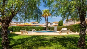 Zona de piscina amb gandules, una palmera i un edifici al fons.