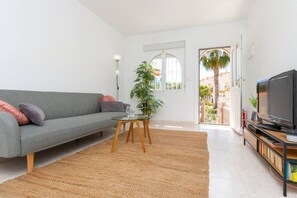 Una sala de estar moderna con un sofá gris, una mesita, un televisor y un ventanal grande.