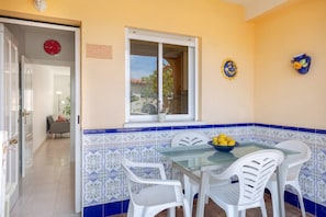 Un comedor con mesa de vidrio, sillas blancas, un bol de limones y ventana con vistas al exterior.