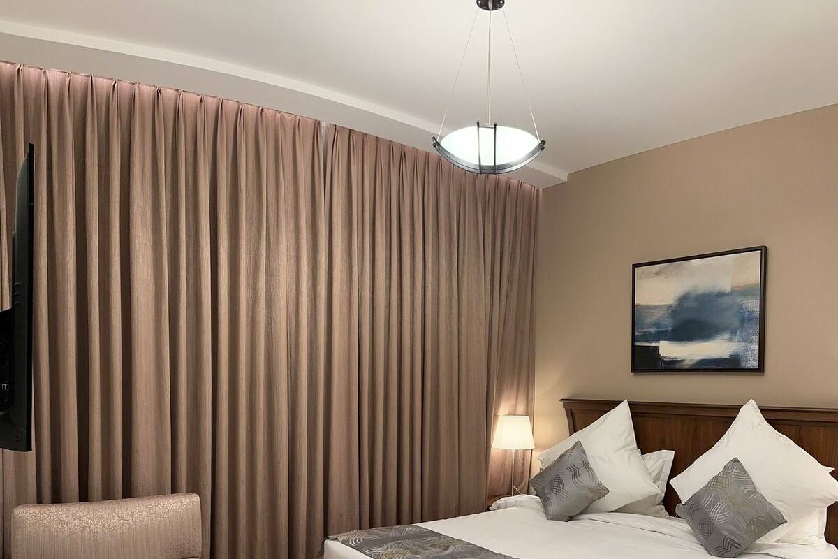 A hotel room with a large bed, a chair, a desk with a lamp, and a painting on the wall.