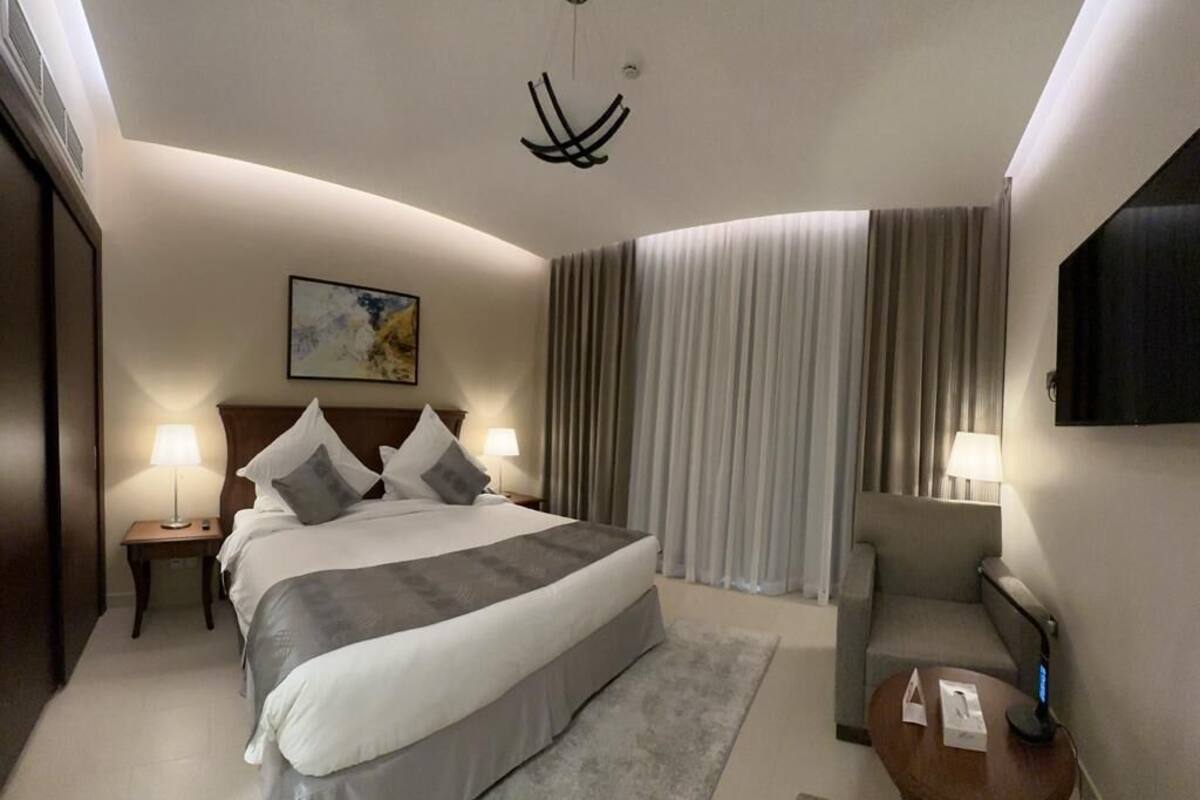 A hotel room with a large bed, two bedside tables with lamps, a chair, a desk, and a large window with curtains.