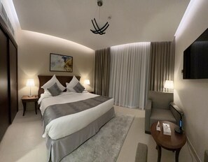 A hotel room with a large bed, two bedside tables with lamps, a chair, a desk, and a large window with curtains.