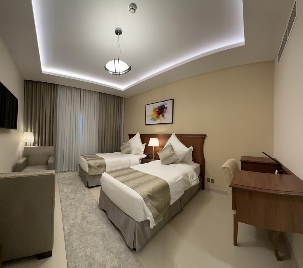 Een hotelkamer met twee bedden, een bureau, een stoel, een lamp en een schilderij aan de muur.