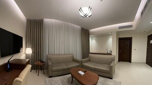 Quarto de hotel moderno com sofá, mesa de centro, TV e luminária.