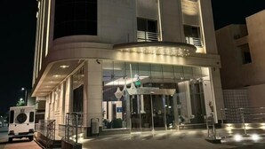 Exterior do Hotel Aldolia à noite, com design moderno, entrada destacada e sinalização iluminada.