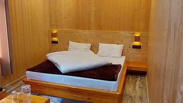 Una habitación con paneles de madera, una cama, mesitas de noche y un pequeño taburete de madera.