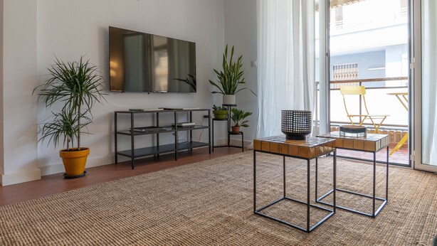 A modern living room with a flat-screen TV, two potted plants, a wooden coffee table, and a sliding glass door leading to an outdoor area. - Amazinn Places - Cabañal Boutique (Valencia)