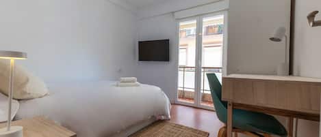 A hotel room with a bed, a desk, a chair, a TV, and a balcony with a view.