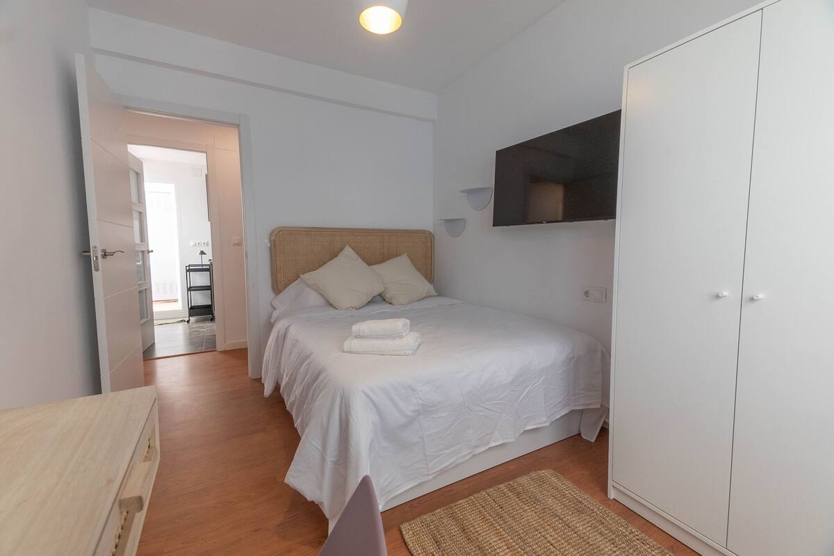 Ein Schlafzimmer mit Bett, Kleiderschrank, Fernseher und einer Tür zu einem anderen Raum.