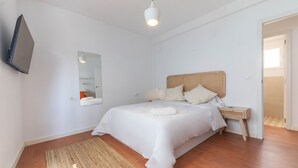 A bedroom with a bed, a bedside table, a mirror, and a television mounted on the wall. - Amazinn Places - Cabañal Boutique (Valencia)
