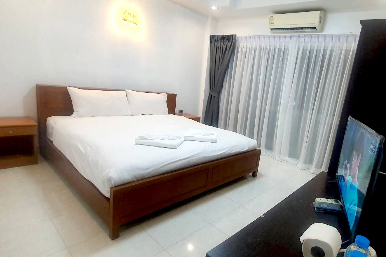 A hotel room with a bed, a TV, a desk with a computer, and a window with curtains.
