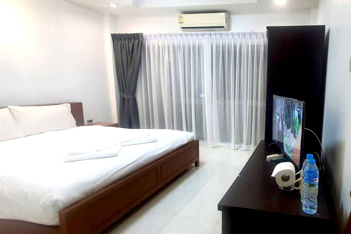 Ein Hotelzimmer mit Bett, Fernseher, Schreibtisch und einer Flasche Wasser sowie einer Klimaanlage.