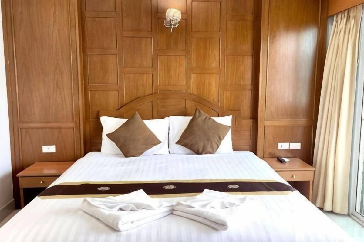 Ein Hotelzimmer mit einem holzverkleideten Kopfteil, einem ordentlich bezogenen Bett mit weißen Leinen, zwei Kissen und einem Nachttisch mit einer Lampe.