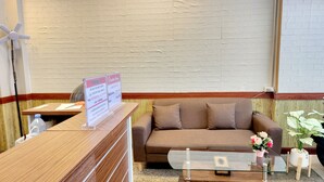Una zona de recepción con un mostrador de madera, un sofá marrón, una mesa de centro de vidrio y una planta en maceta.
