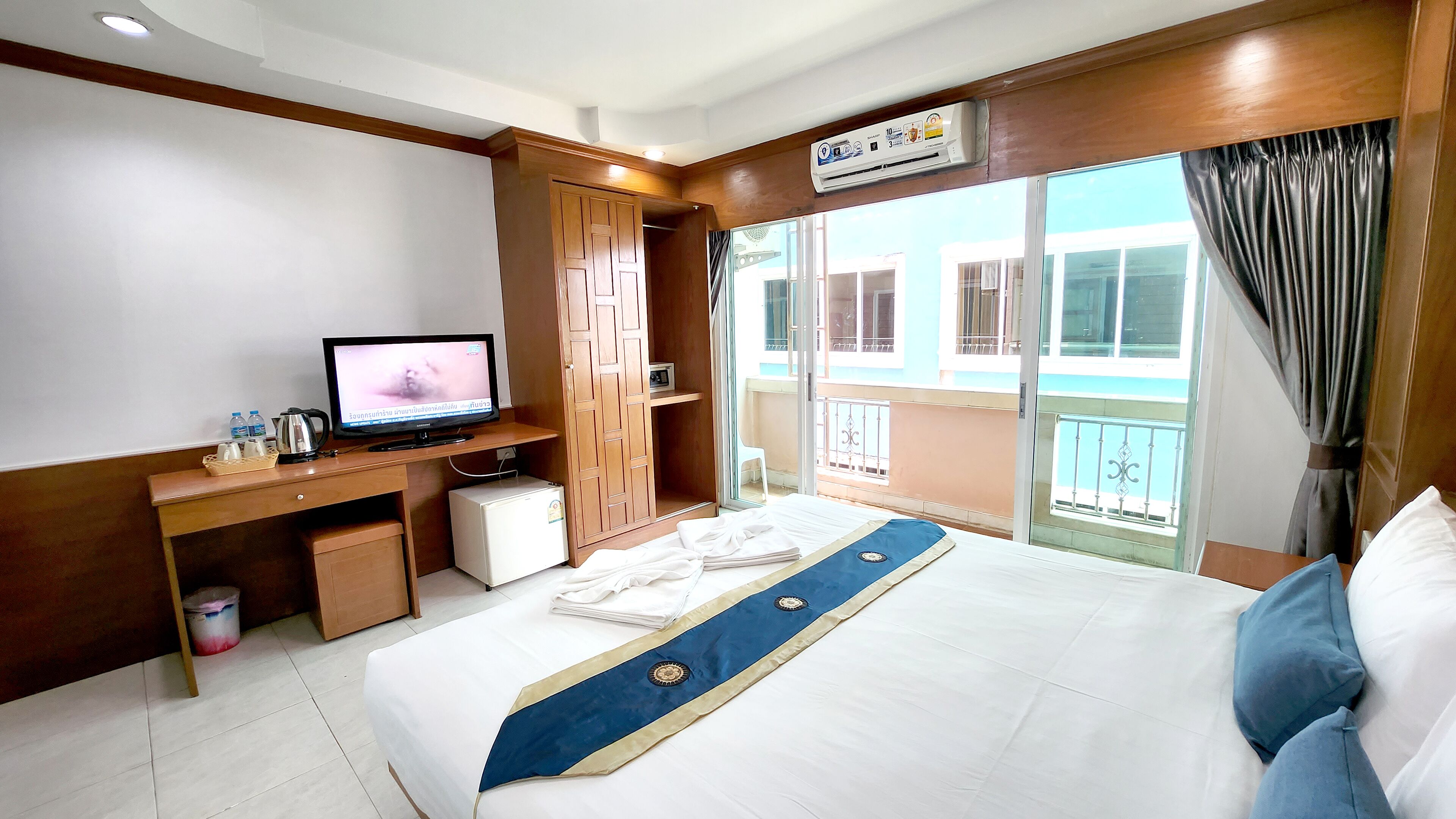 A hotel room with a bed, a desk with a computer, a small refrigerator, and a window with a view of the outside.