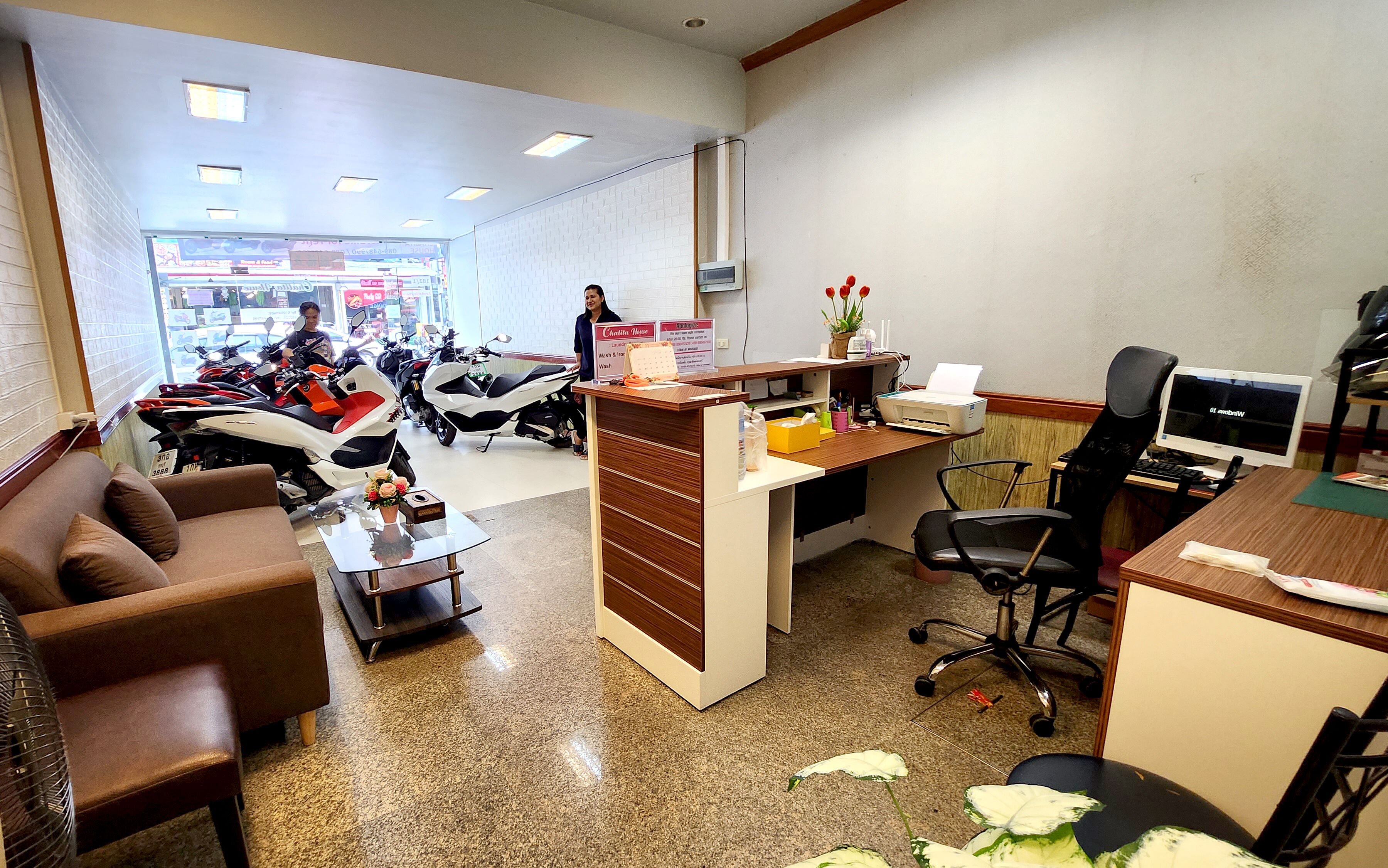 A reception area with a counter, office chairs, a computer, and a view of parked motorcycles outside.