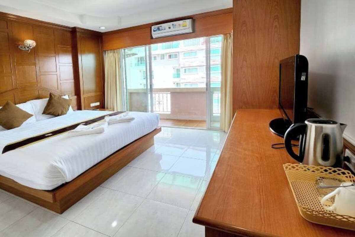 A hotel room with a large bed, a wooden desk with a kettle, and a TV.