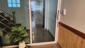 Un pasillo con una puerta de vidrio que da a una escalera, una planta en maceta y un dispositivo fijado a la pared.