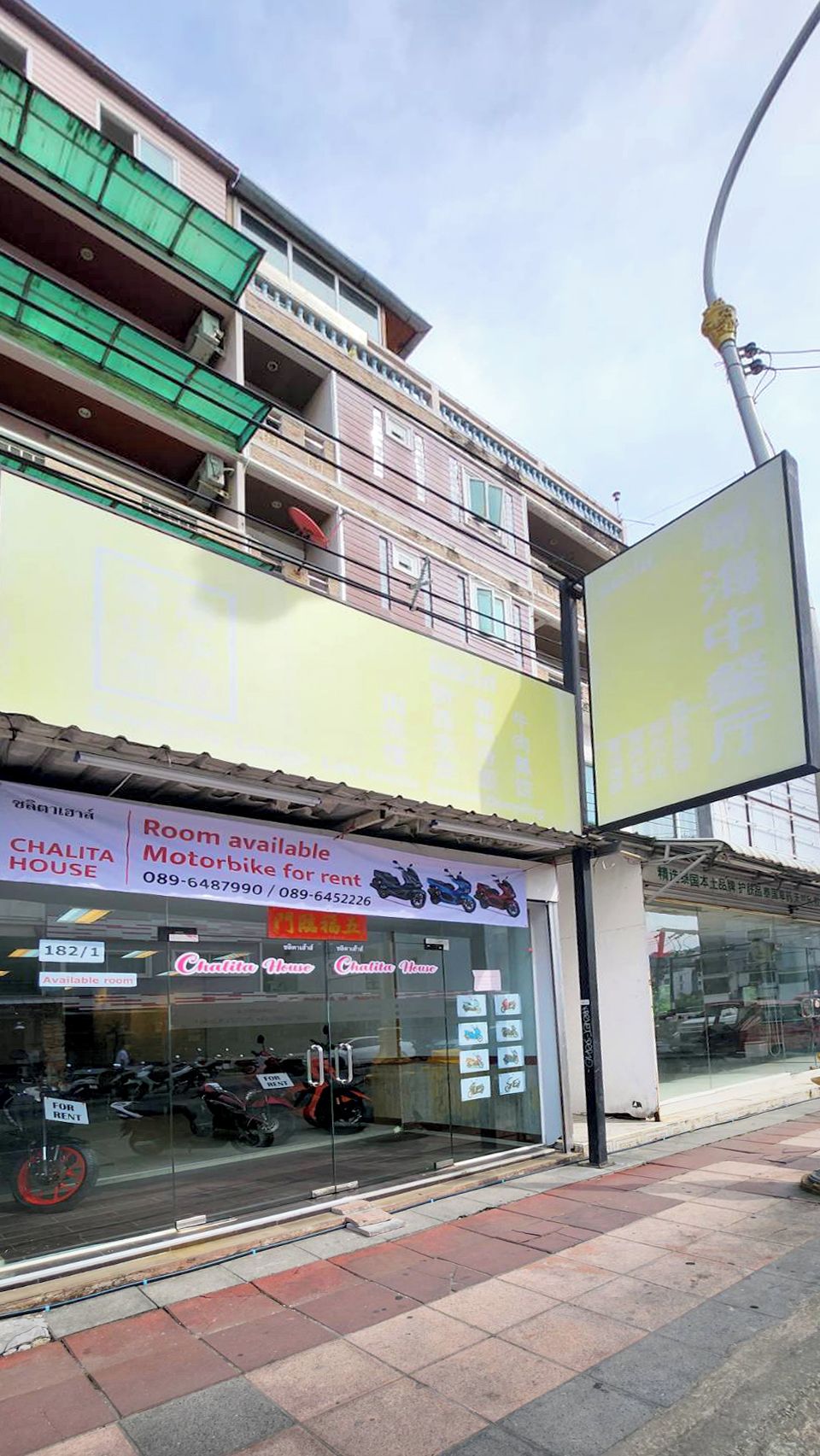 Un edificio con un cartel que anuncia la disponibilidad de habitaciones para alquiler y una motocicleta.