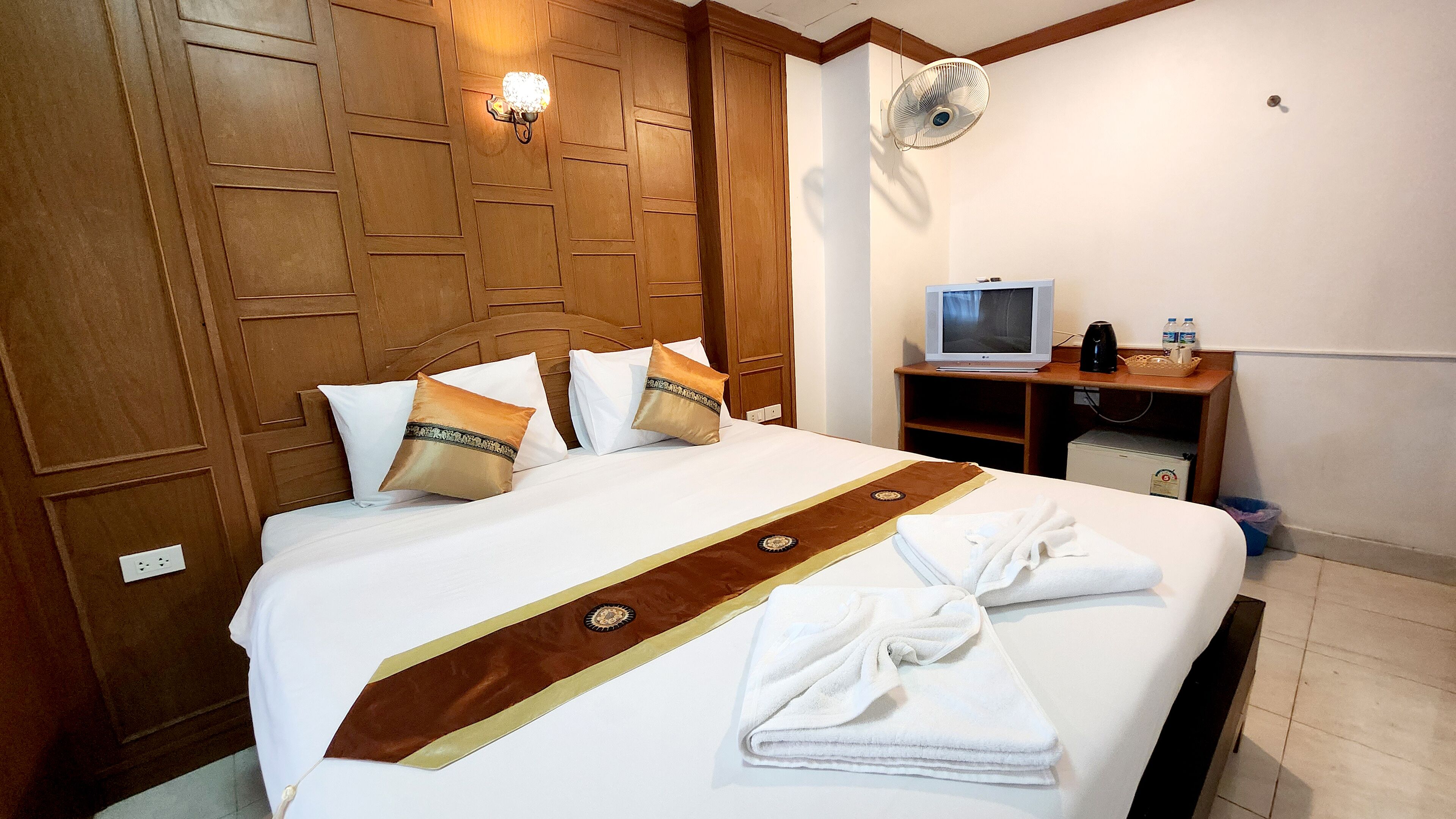 Habitación de hotel con cabecera de madera, televisor de pantalla plana, escritorio con cafetera y toallas sobre la cama.