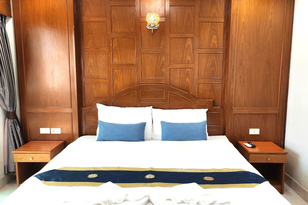 Ein Hotelzimmer mit einem hölzernen Kopfteil, einem Bett mit weißblauer Bettwäsche und zwei Nachttischen mit Lampen.