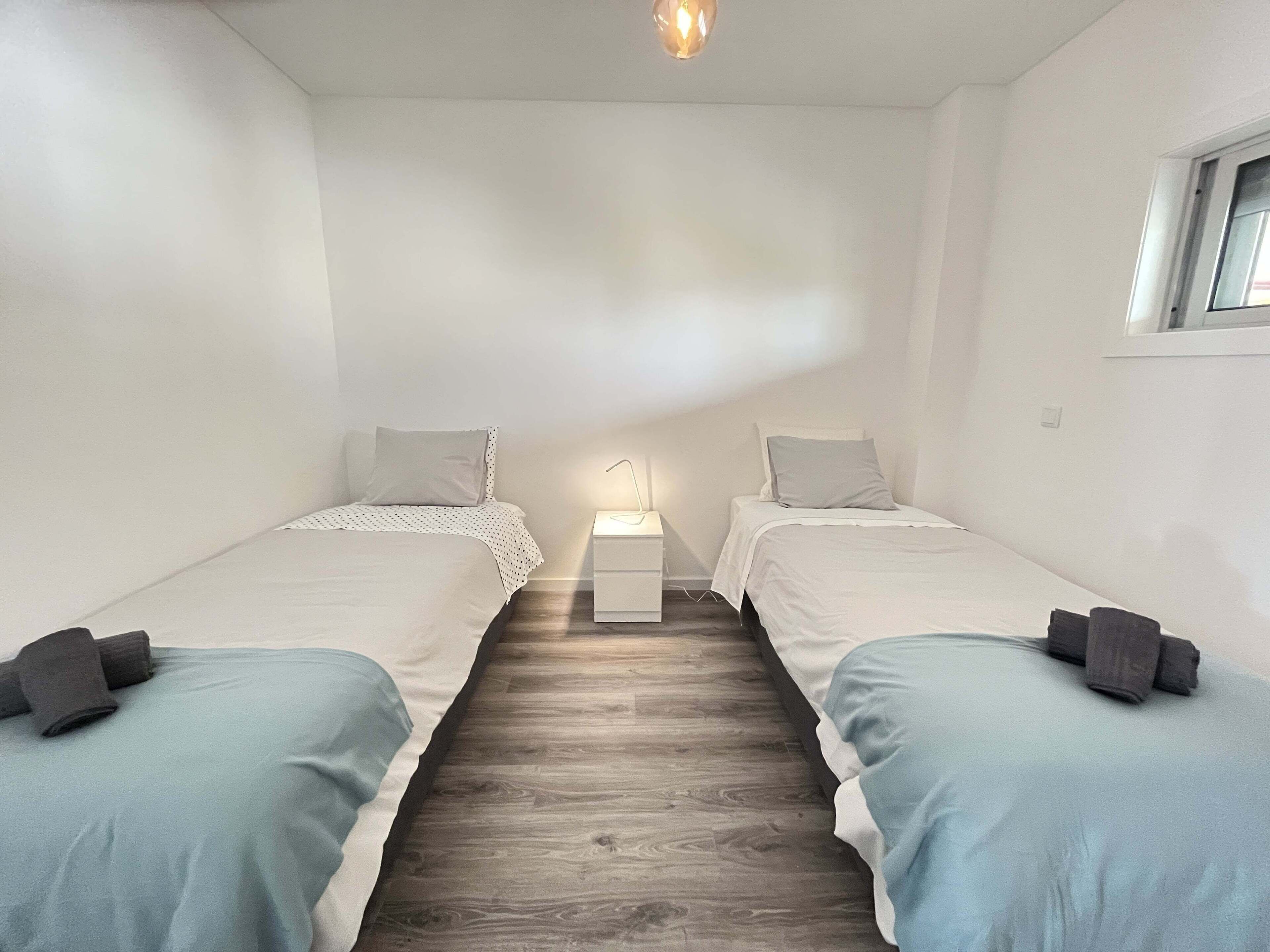 Une chambre avec deux lits simples, une petite table de chevet avec une lampe et une fenêtre sur le mur de droite.