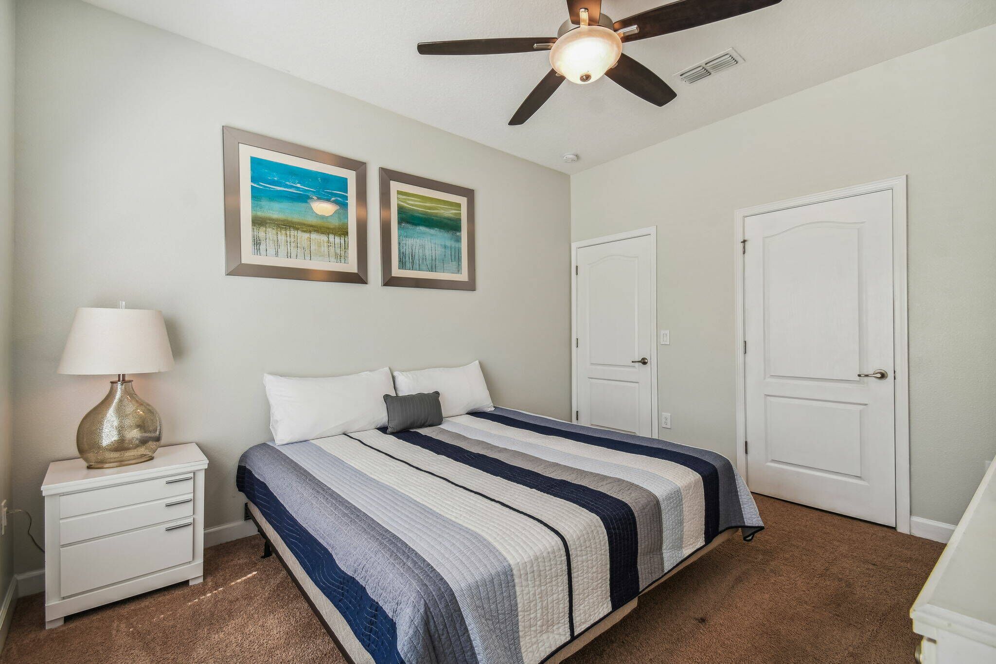 A bedroom with a bed, nightstand, lamp, ceiling fan, and two doors.