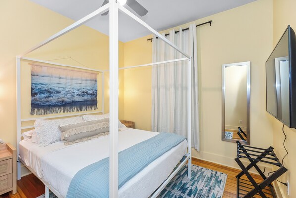 Un dormitorio con cama con dosel, un cuadro grande, un espejo y un televisor montado en la pared.