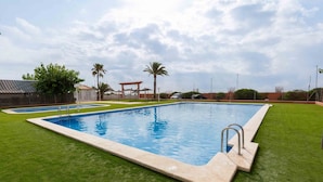 Una piscina rectangular con borde de azulejos, rodeada de césped verde y cuidado.