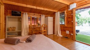 Habitación de cabaña de madera con una cama, un escritorio, una silla y un refrigerador pequeño.