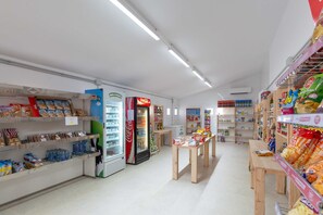 A clean, well-organized store with shelves stocked with snacks, a Coca-Cola refrigerator, and a wooden table in the center.