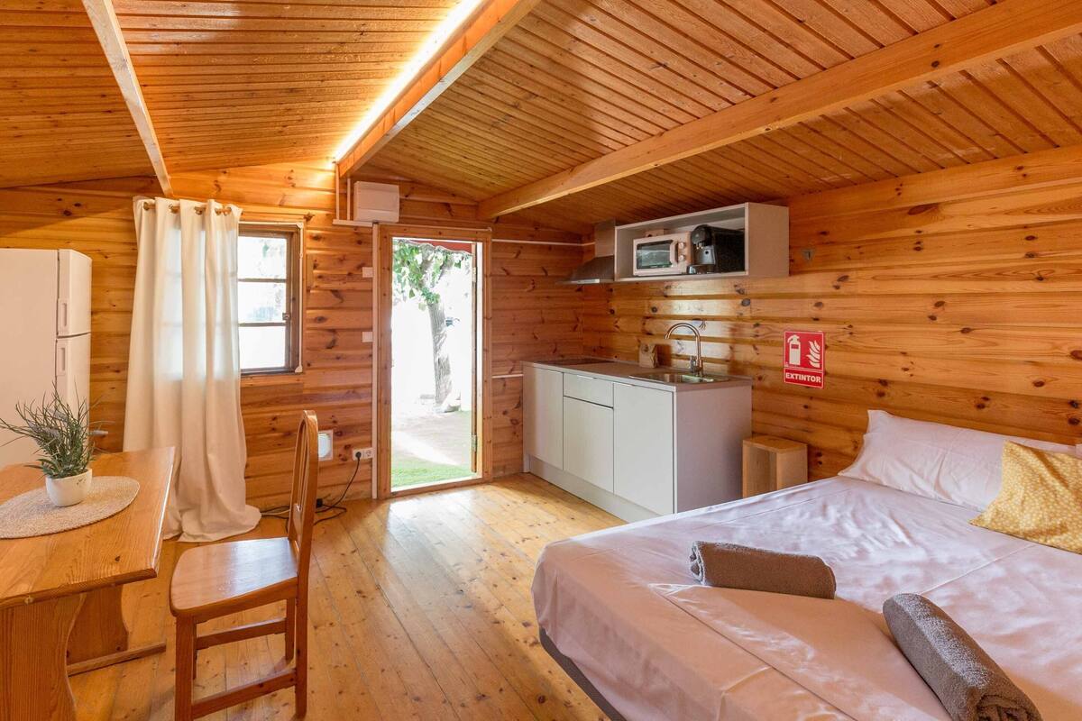 Een houten hutje met een bed, een kleine kitchenette en een eethoek.