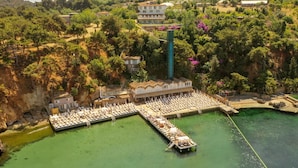 An aerial view of a coastal resort with a swimming pool, lounge chairs, and a pier. - The Roof ADA (Adalar)