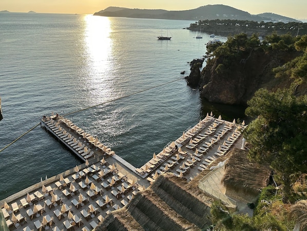 A coastal hotel with a terrace overlooking the sea, featuring rows of sun loungers and umbrellas. - The Roof ADA (Adalar)