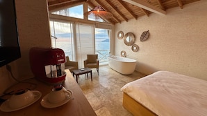 A bedroom with a large window, a bathtub, and a coffee maker. - The Roof ADA (Adalar)