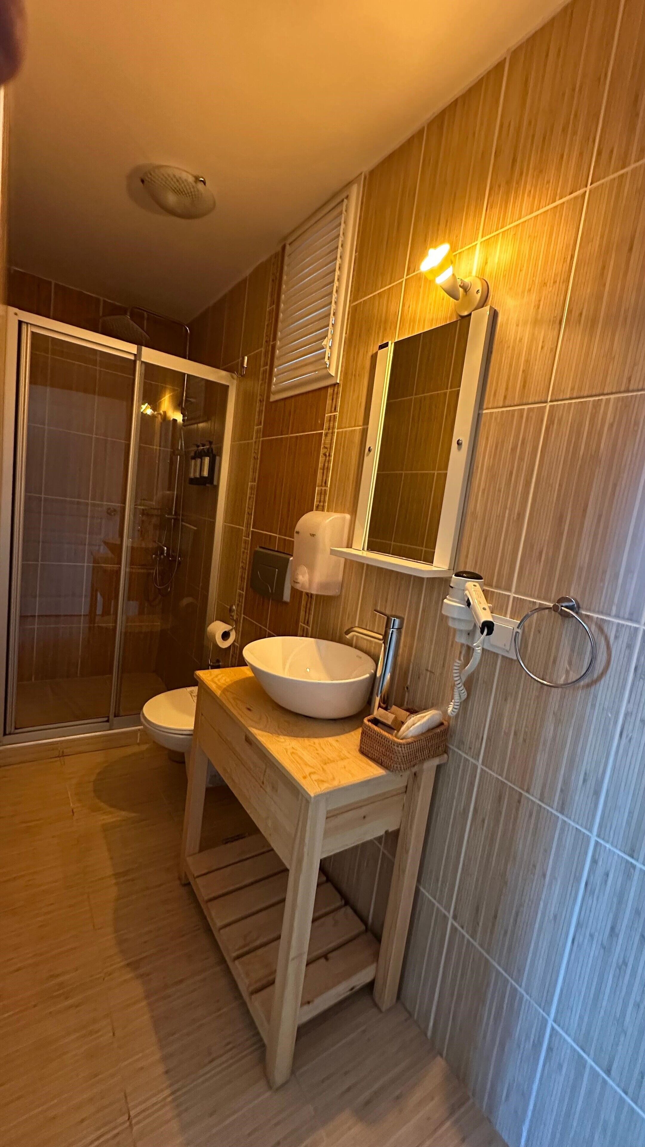 A bathroom with a wooden vanity, a sink, a toilet, and a shower area.