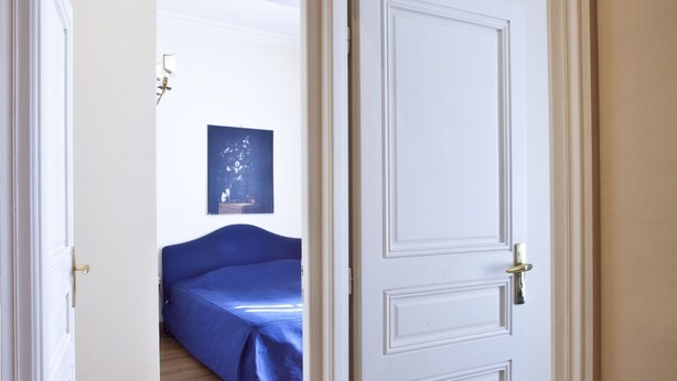 A room with a wooden floor, a bed with a blue cover, and a white door. - Two Bedrooms Flat Close Place Vendome (Paris)