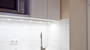 A modern kitchen with white cabinetry, a stainless steel sink, and a microwave above the countertop. - Two Bedrooms Flat Close Place Vendome (Paris)