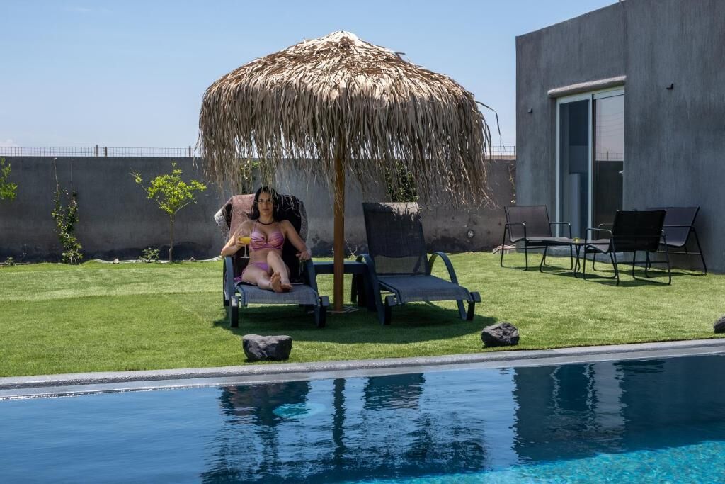 A poolside area with a thatched umbrella, lounge chairs, and a modern building in the background.