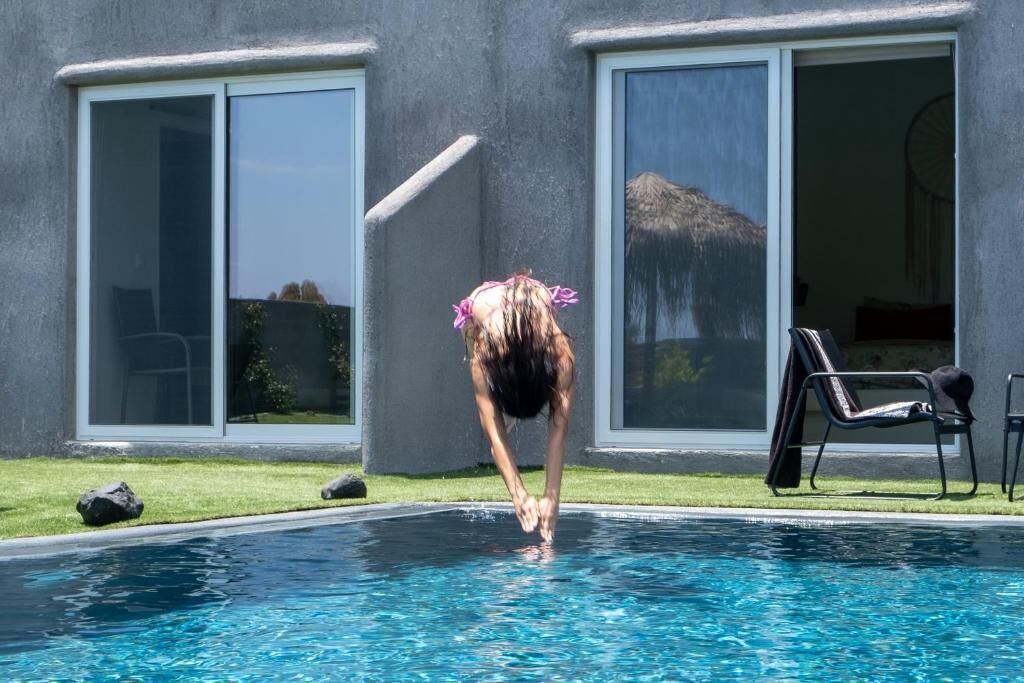 A person diving into a swimming pool with a house in the background.