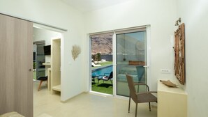 A modern room with a sliding glass door leading to a pool area, a chair, and a wooden cabinet. - Sagma Villas (Santorini)