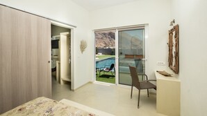 A modern bedroom with a sliding glass door leading to a pool area. - Sagma Villas (Santorini)