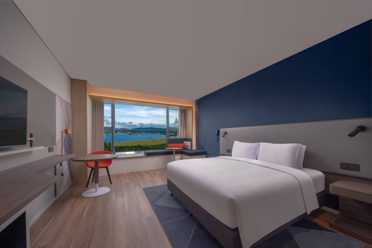 Ett modernt hotellrum med en stor säng, ett skrivbord och utsikt över en sjö.