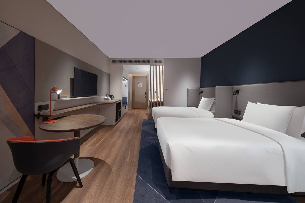 Ett modernt hotellrum med en stor säng, ett skrivbord med en stol, en TV och ett badrum som syns genom en dörr.