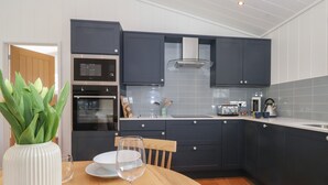 A modern kitchen with dark cabinets, a microwave, oven, and a coffee maker. - Hawthorn Croft (Ulverston)