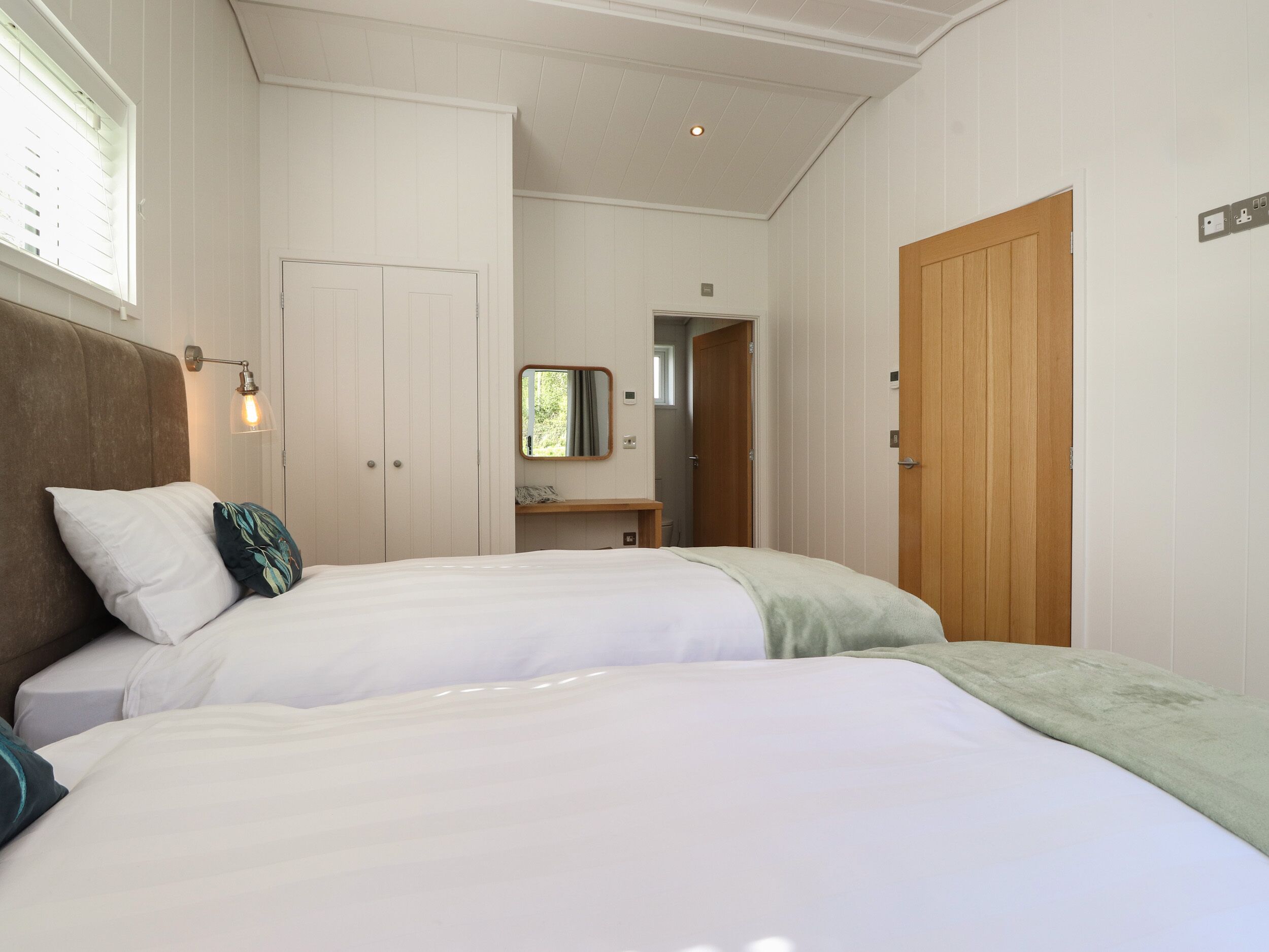 A bedroom with two beds, a wooden door, a mirror, and a bedside lamp.
