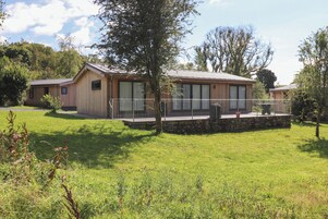 Una cabaña moderna de madera con cimientos de piedra, ventanas amplias y un espacio exterior cubierto.