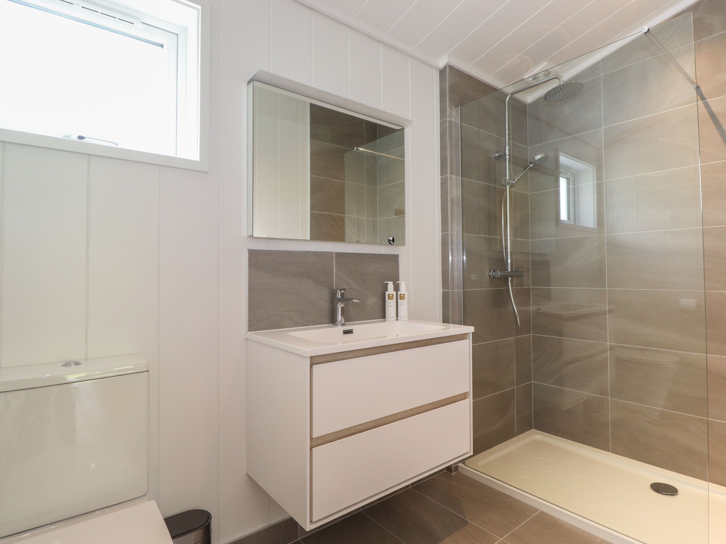 A modern bathroom with a glass shower enclosure, a white vanity with a mirror, and a toilet.